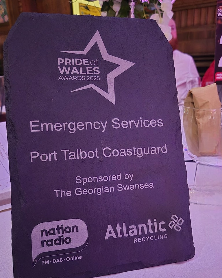 A slate award sits on a table. Etched on the award reads 'Pride of Wales Awards 2025, Emergency Services, Port Talbot Coastguard'