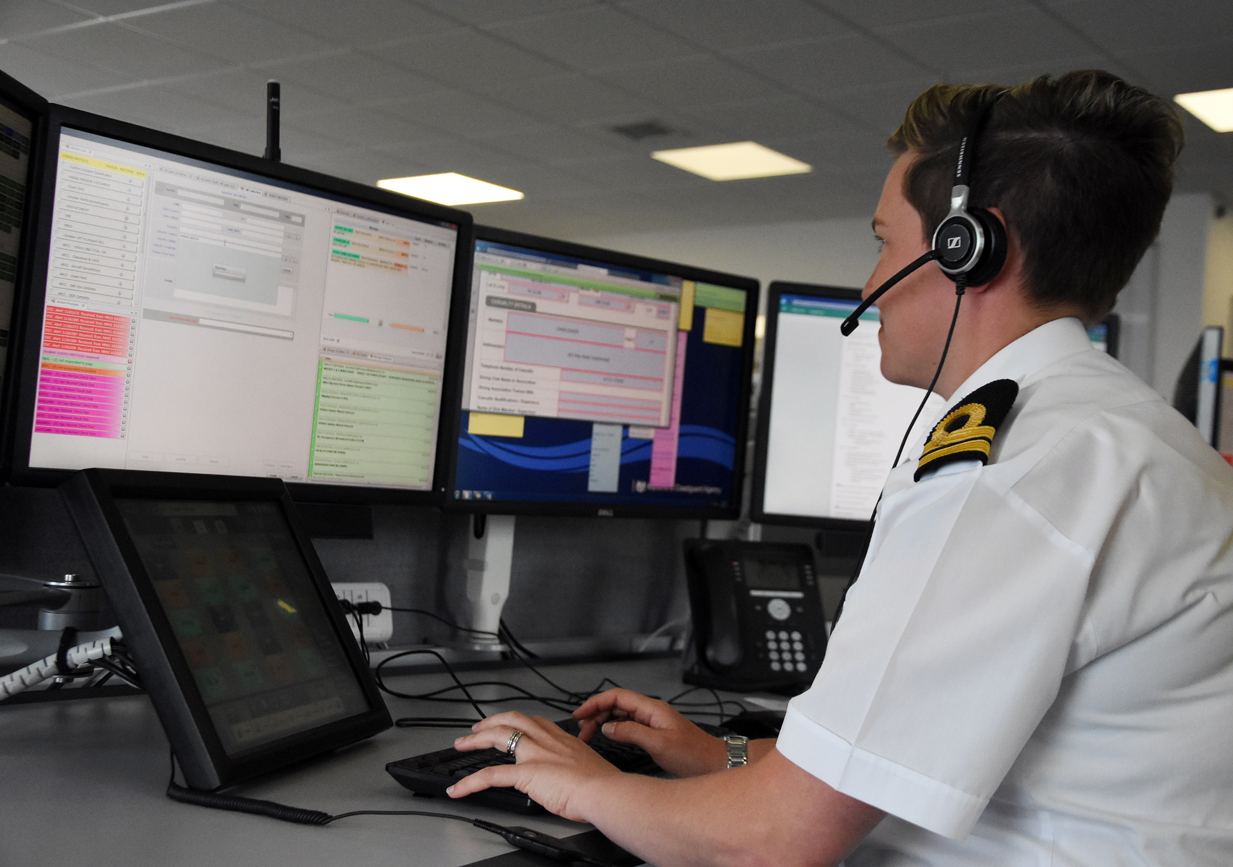 Jolene in white shirt HM Coastguard uniform in front of bank of computer monitors