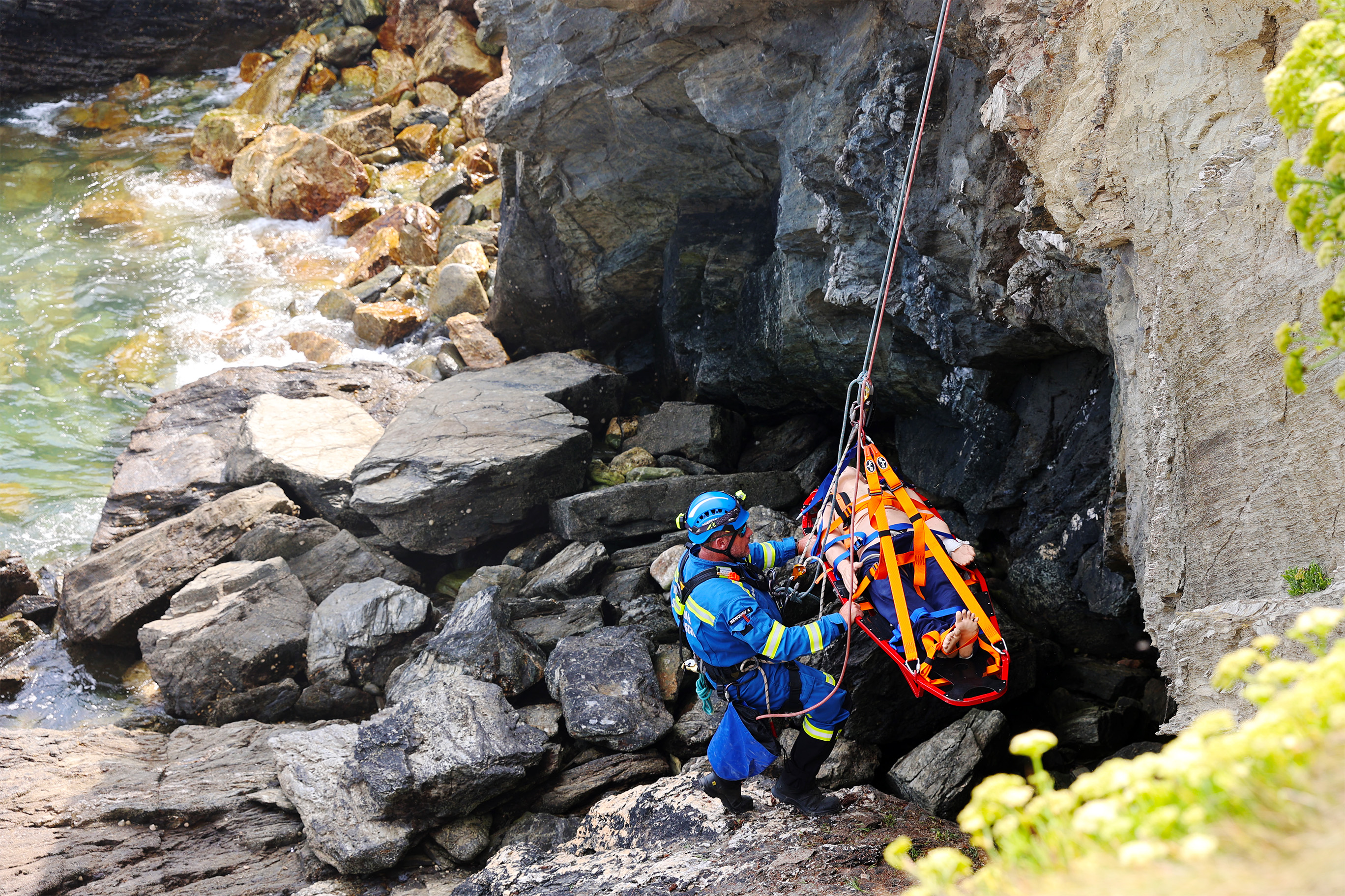 At the foot of a cliff, a Coastguard Rescue Officer prepares a stretcher containing a dummy