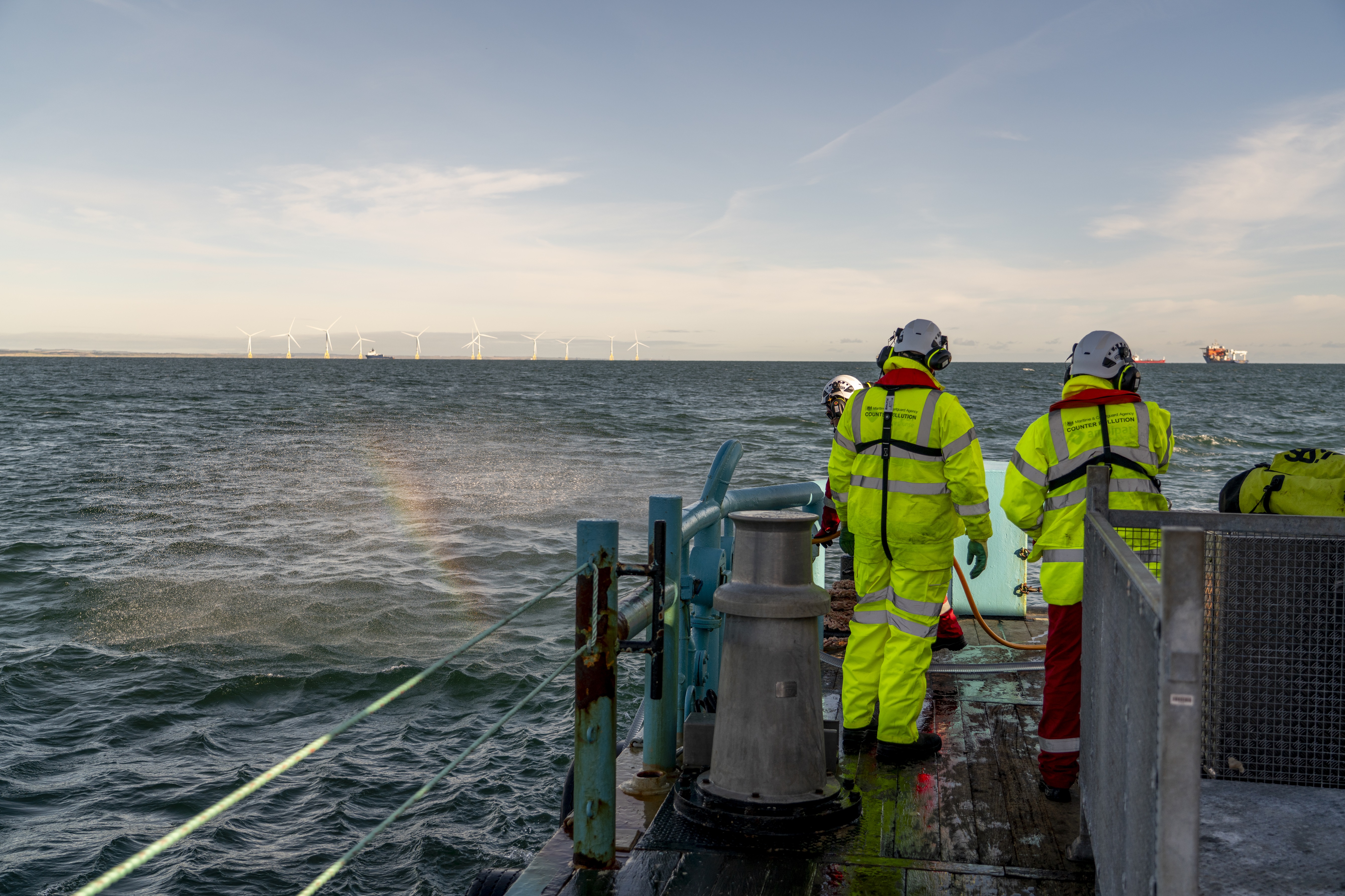Two men in hi-viz outfits look across the sea from the back of a work boat
