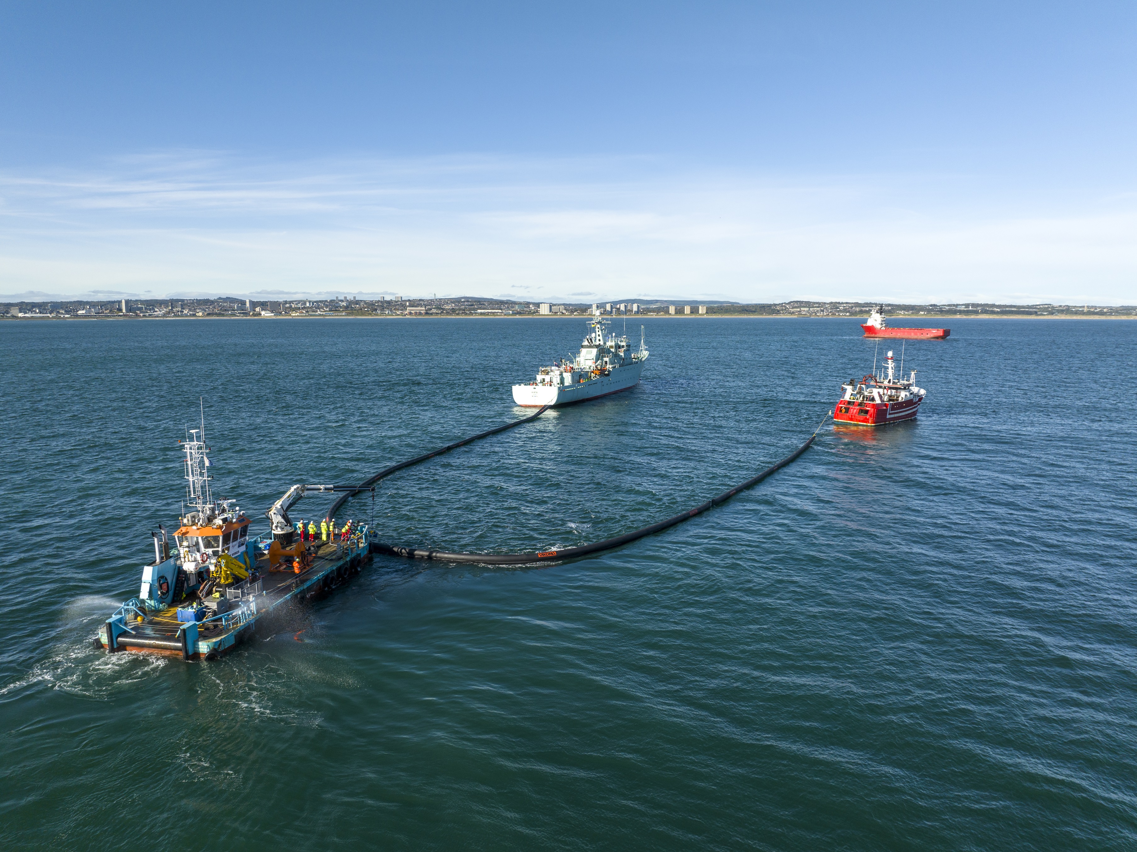 Three vessels maneuver a counter pollution boom into place