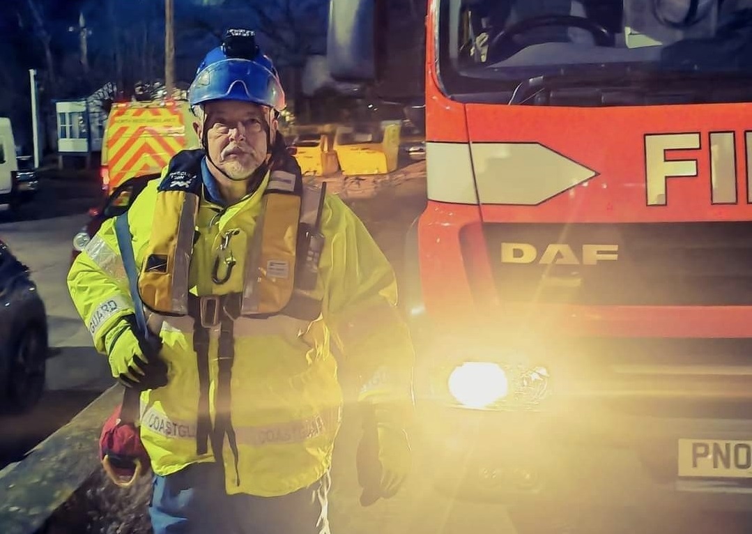 HM Coastguard Fleetwood Coastguard Rescue Team member Alan walks in safety uniform alongside a Fire Service vehicle.