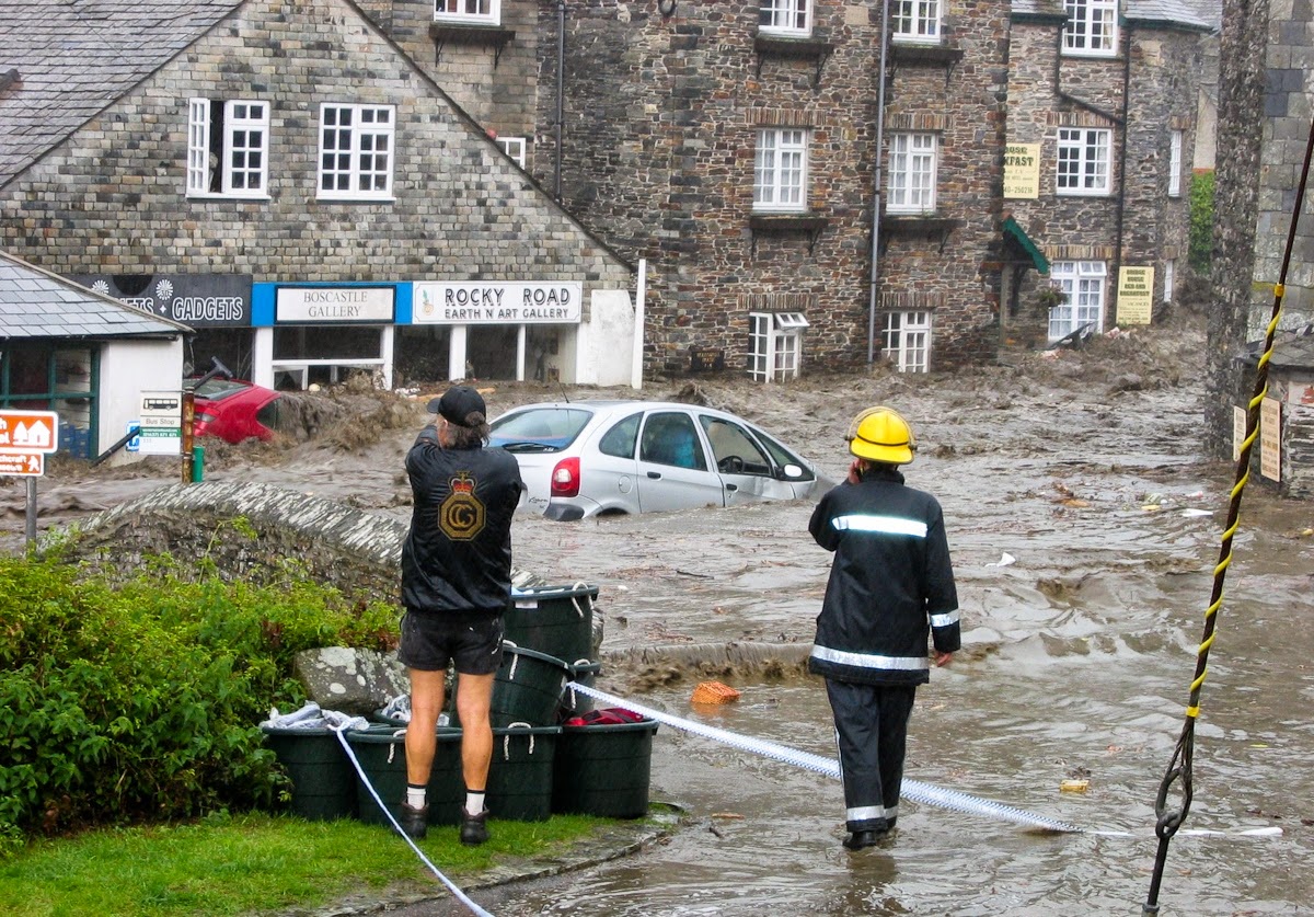 A coastguard and firefighter observe a car being swept past by floodwater