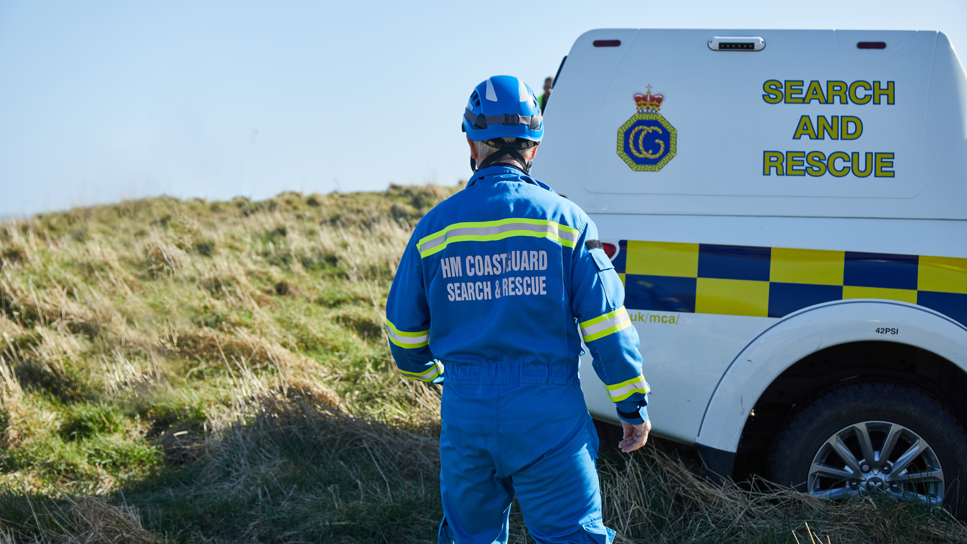 A coastguard stands in front of a rescue vehicle by a cliff