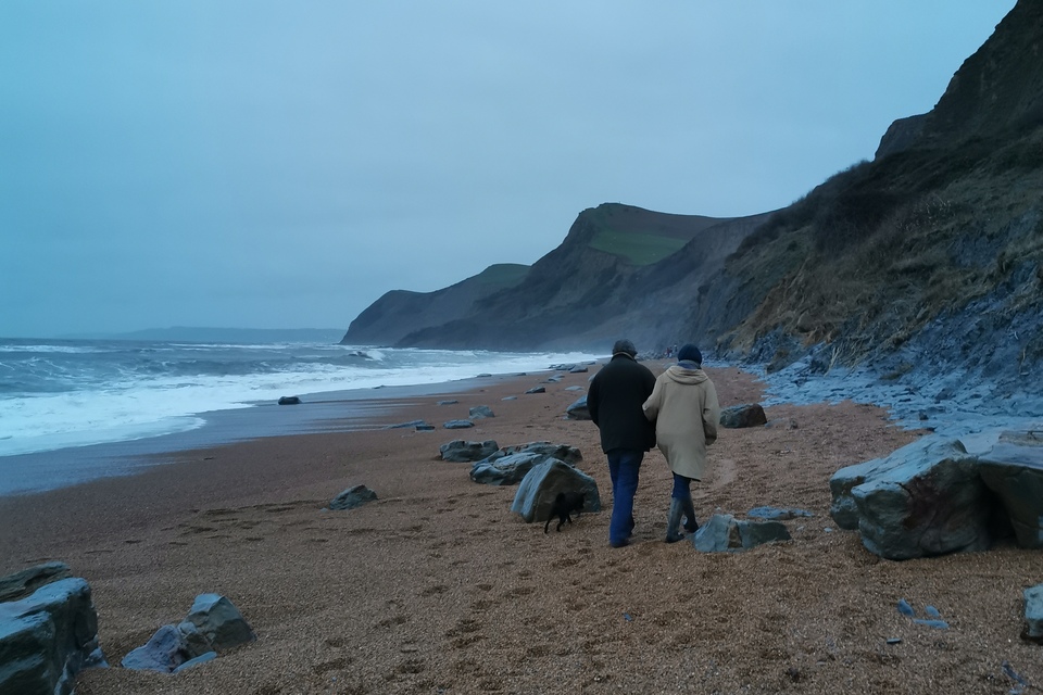 A couple walking along a pebbled beach in winter