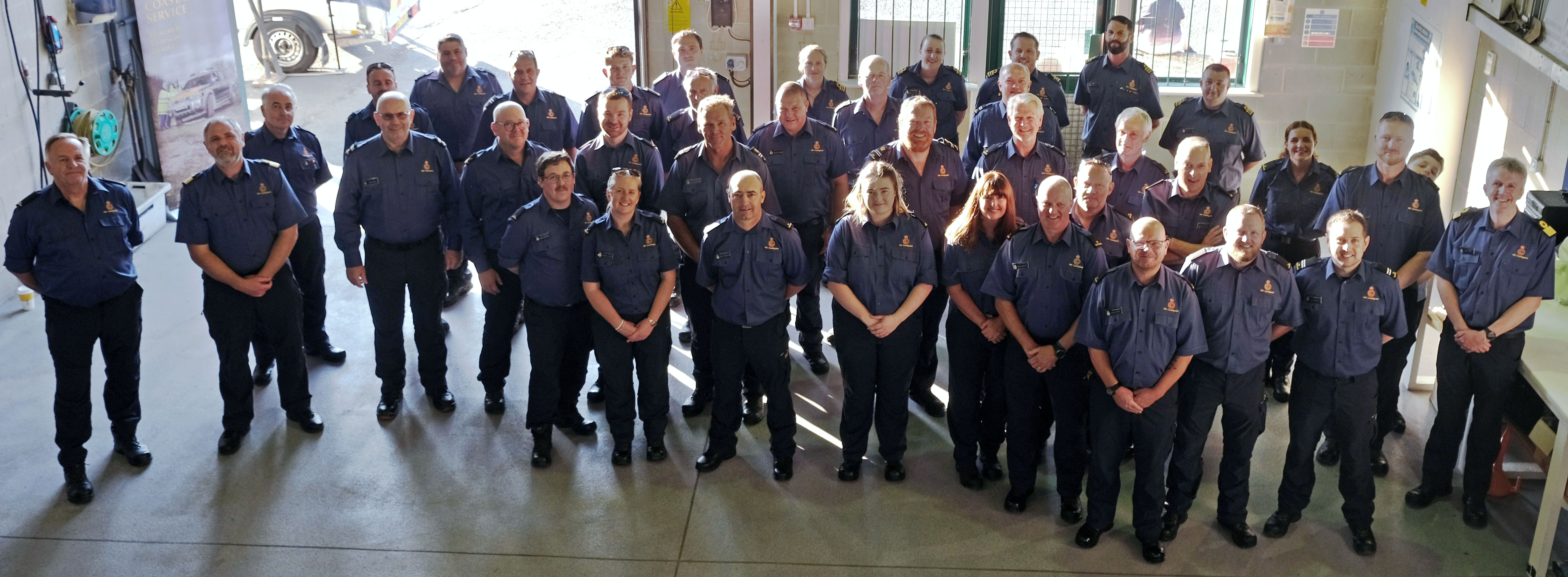 A large group of HM Coastguard representatives stood looking up towards the camera
