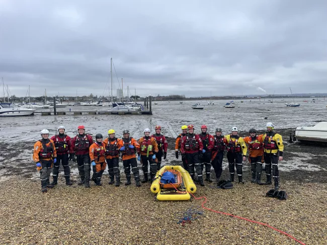Members of HM Coastguard and Hampshire and Isle of Wight Fire and Rescue Service smiling for a photo with kit and equipment, after mud rescue training in Portsmouth
