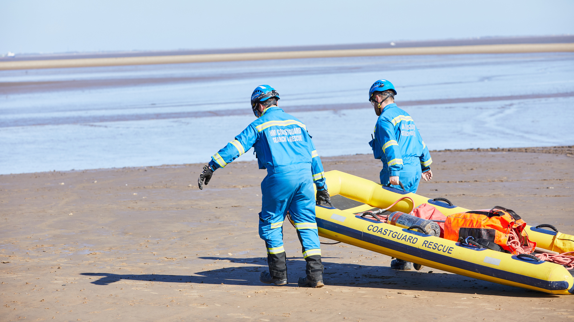 Two coastguards drag a rescue sled over sand