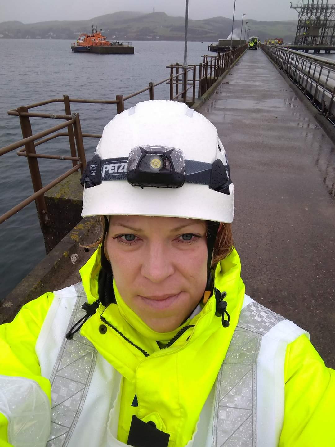 Female in high vis and PPE taking selfie on dock/pier with RNLI lifeboat in background