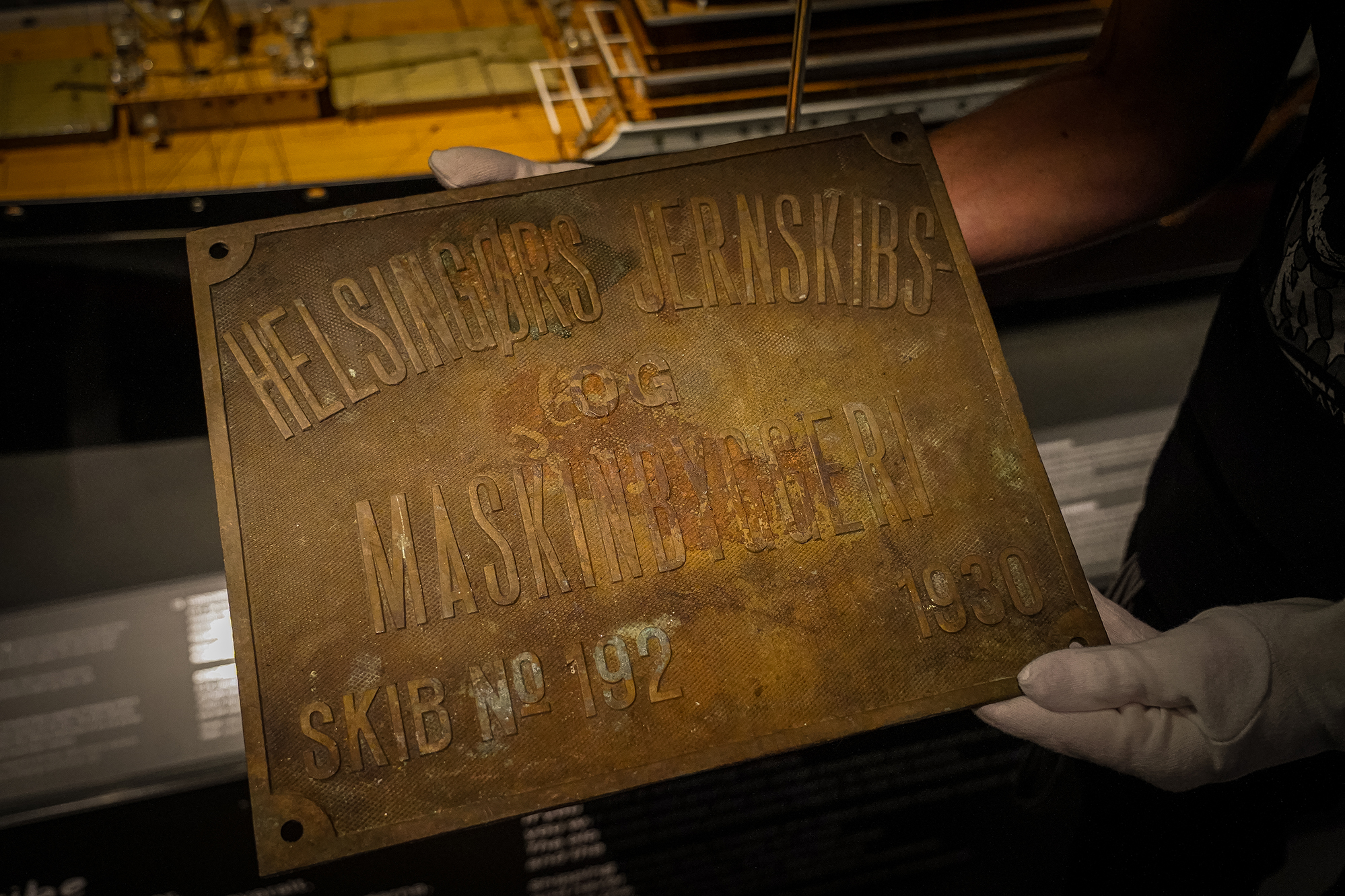 Two gloved hands hold the rusty maker's plate of the SS Birgitte