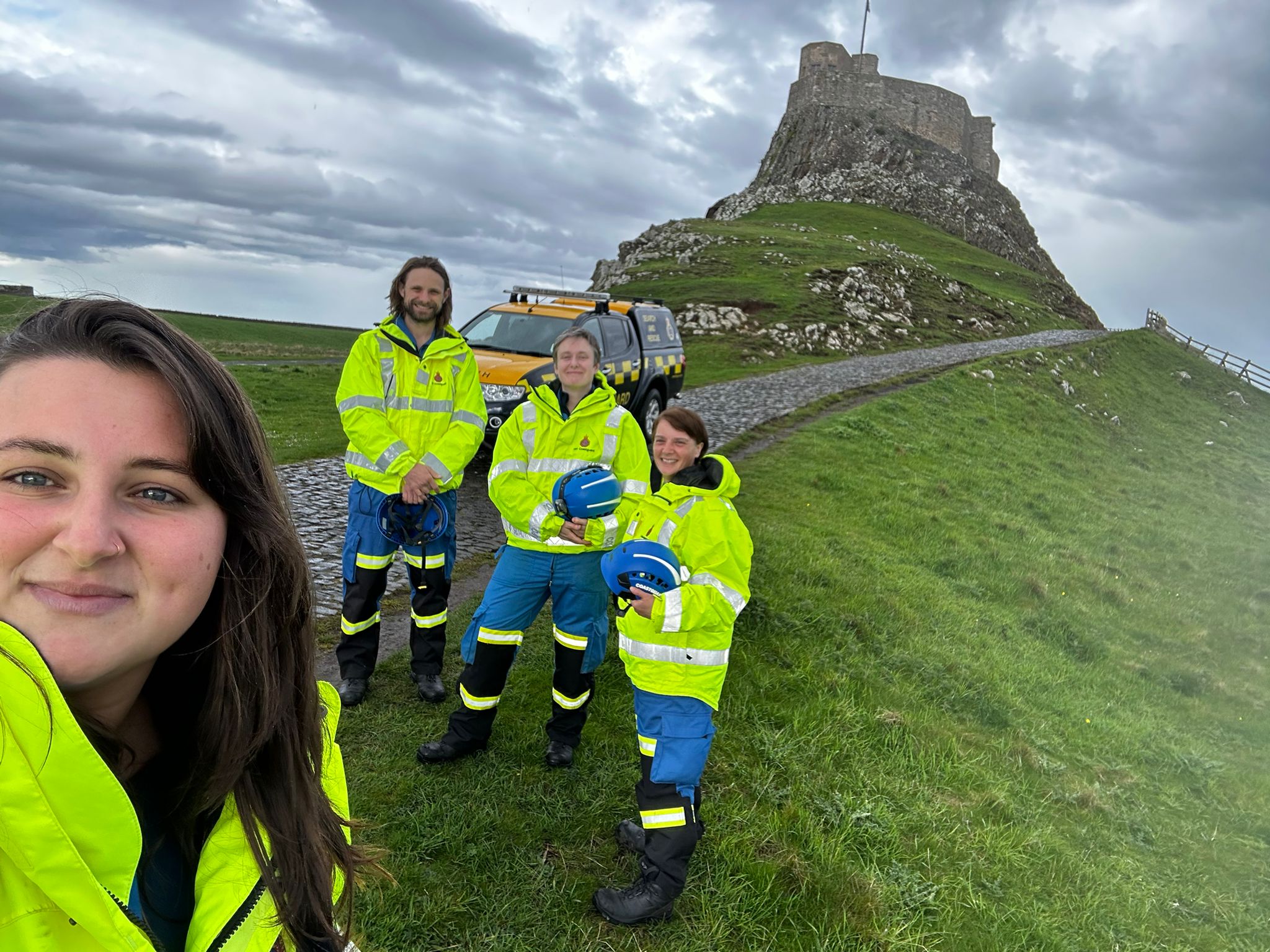 Coastguard Rescue Officer Molly Luke and her team smiling, with Lindisfarne Castle in the background 