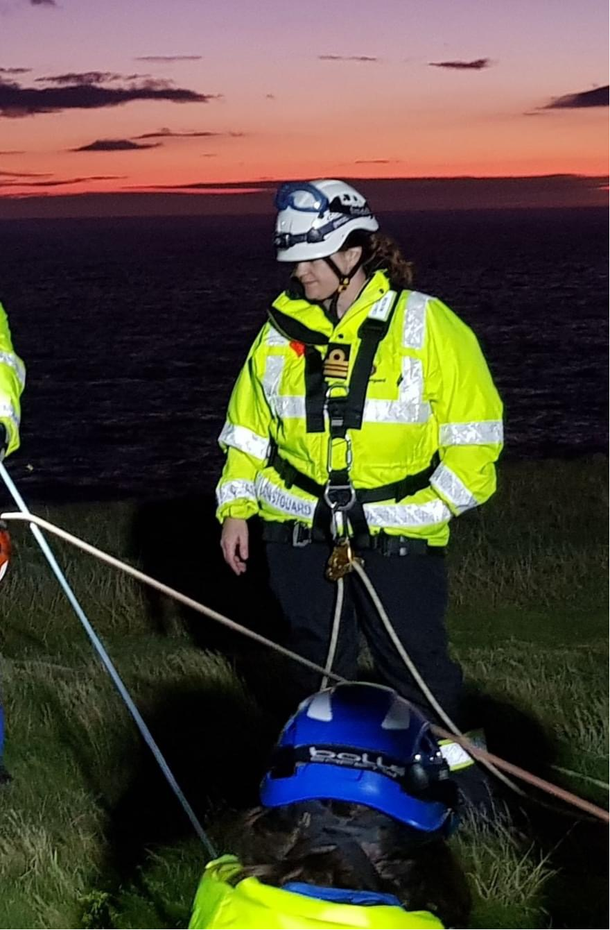 Nicola Davies in a hi-viz jacket is clipped into a rope system at the top of a cliff