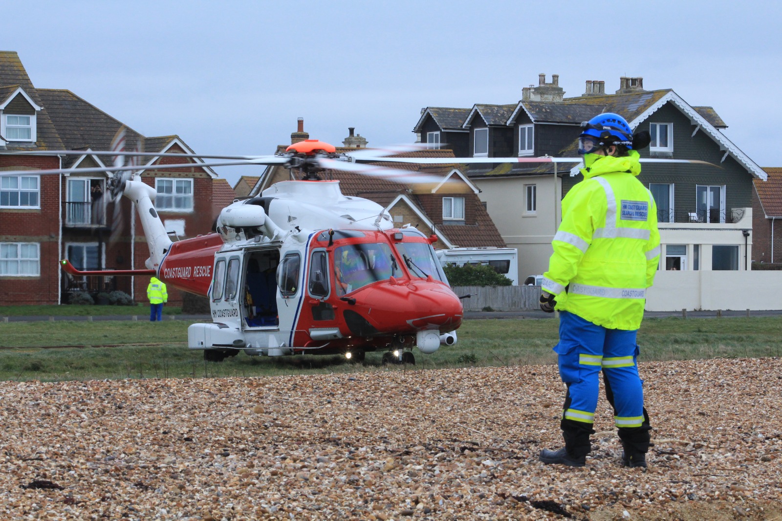 Coastguard Rescue Officer Olivia Letchford with her back to camera, facing the direction of a Coastguard helicopter 
