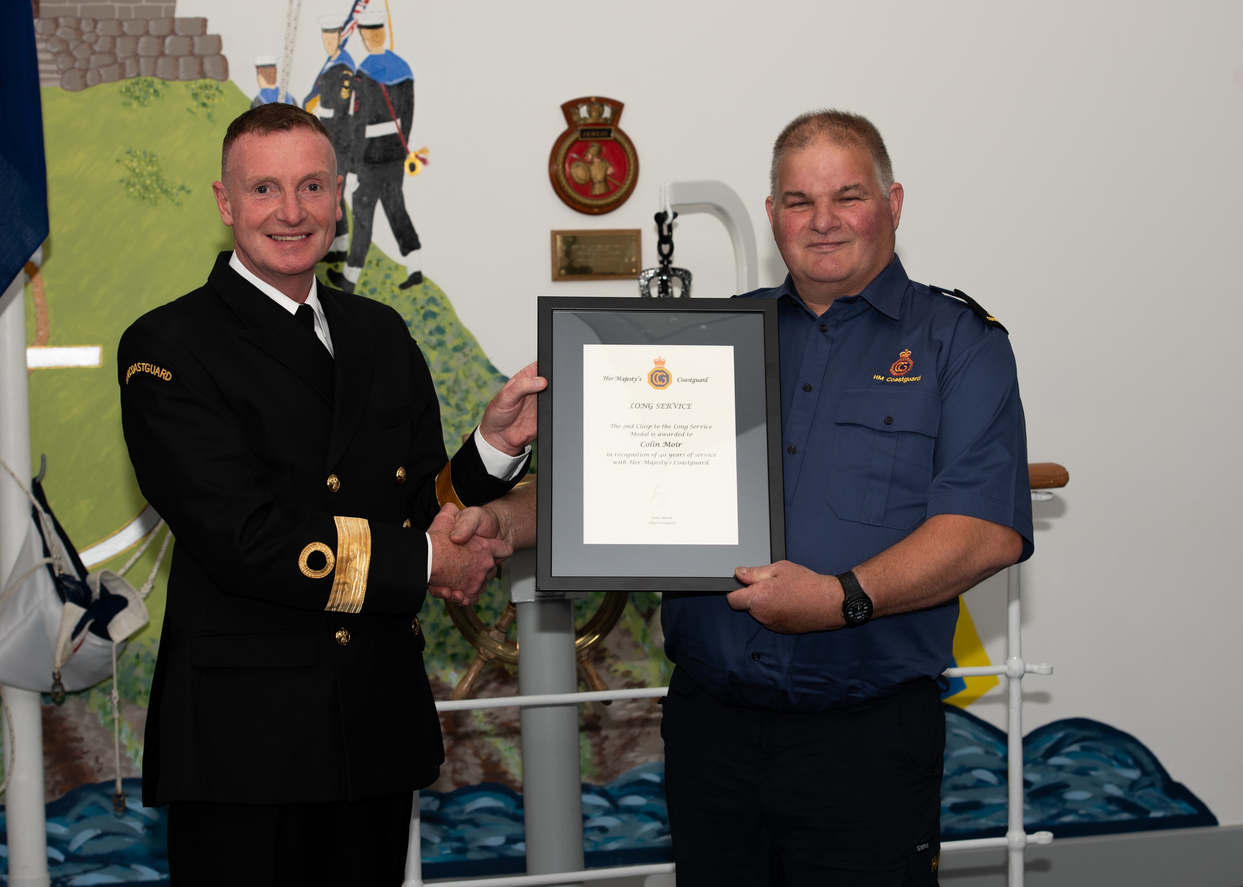 Pat O'Callaghan  shakes hands with Colin Moir, holding a framed long service certificate