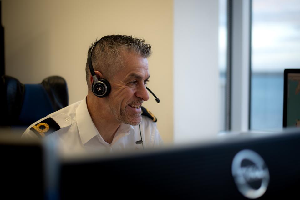 Maritime call handler smiling behind a bank of computers in Coastguard uniform