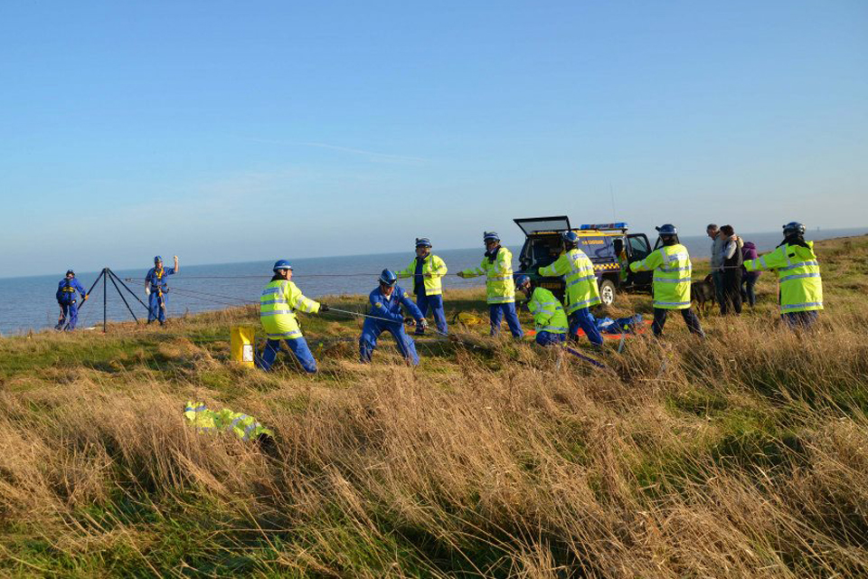 Coastguards haul on rope at the top of a cliff