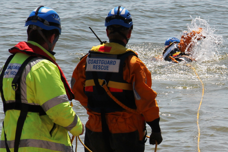 Two coastguards hold a tether connected to a third coastguard swimming from the shore
