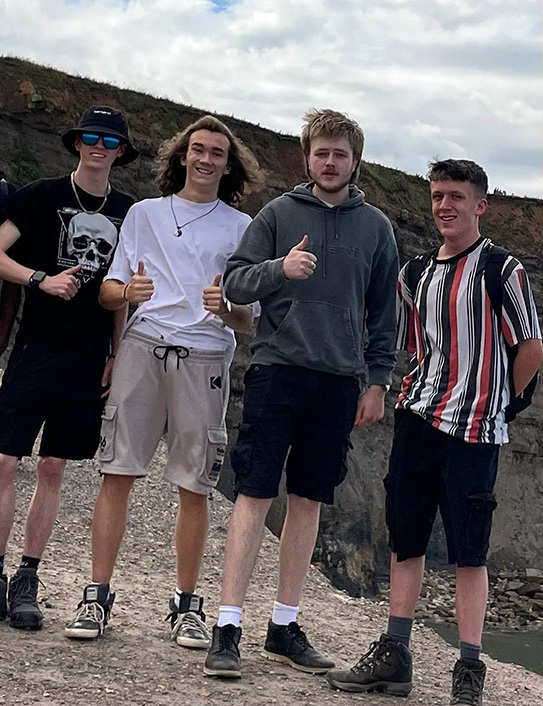 Loughborough friends Josh, Alfie, Luke and Joe stand at the foot of clifftops under cloudy skies in Whitby