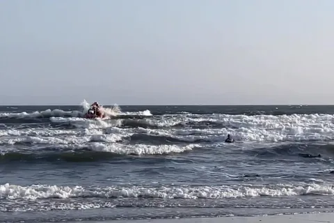 Swimmer in sea with breaking waves and a small lifeboat in distance