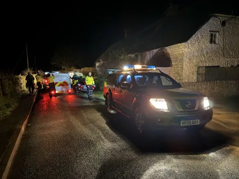 An HM Coastguard vehicle with blue light on, parked in a road at night