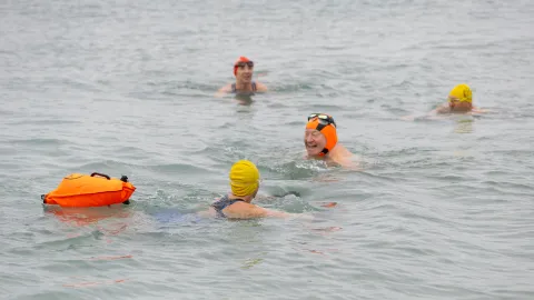 Swimmers in the sea wearing bright headcaps and one towing a float