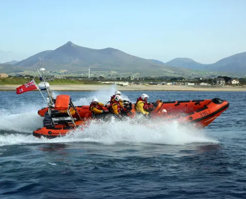 orange lifeboat speeding through the water with mountains in the distance