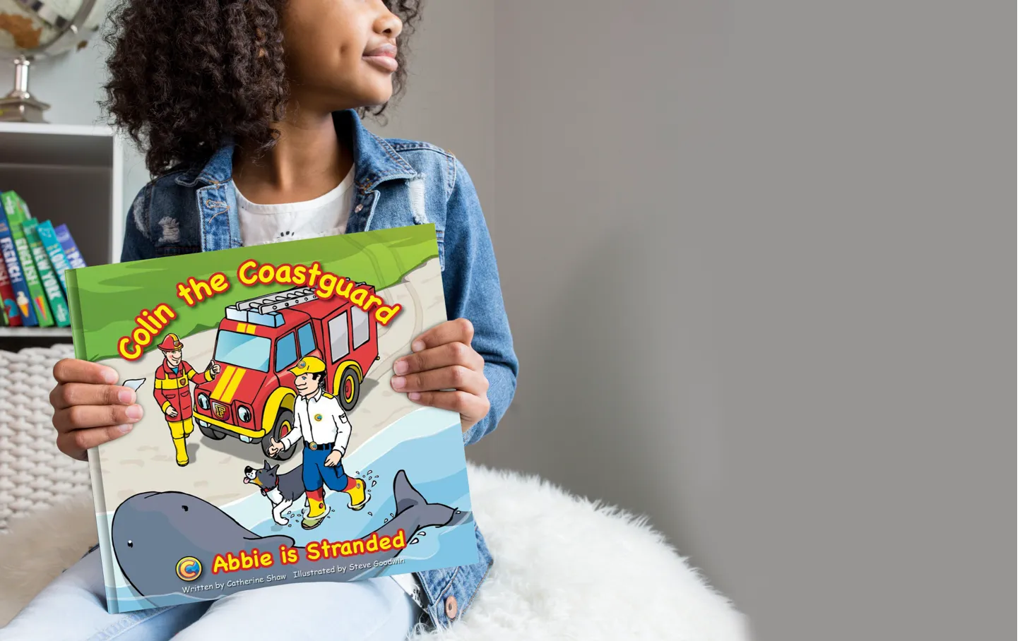 A young girl sitting holding a Colin the Coastguard book in her hands