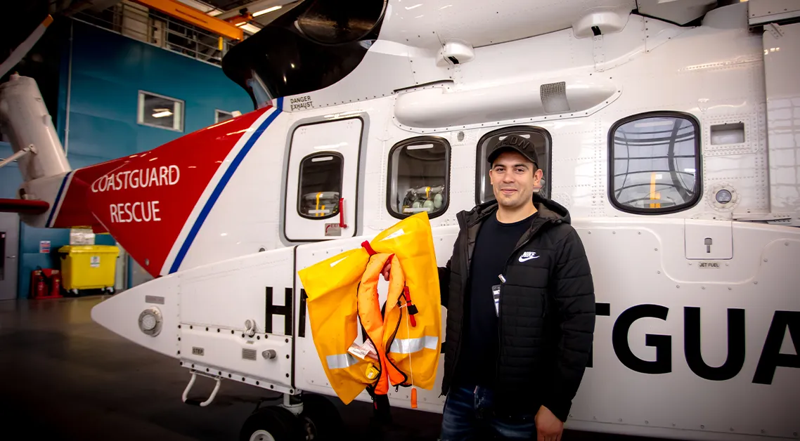 Fisherman holding up his PFD after rescue, stood in front of a HM Coastguard helicopter