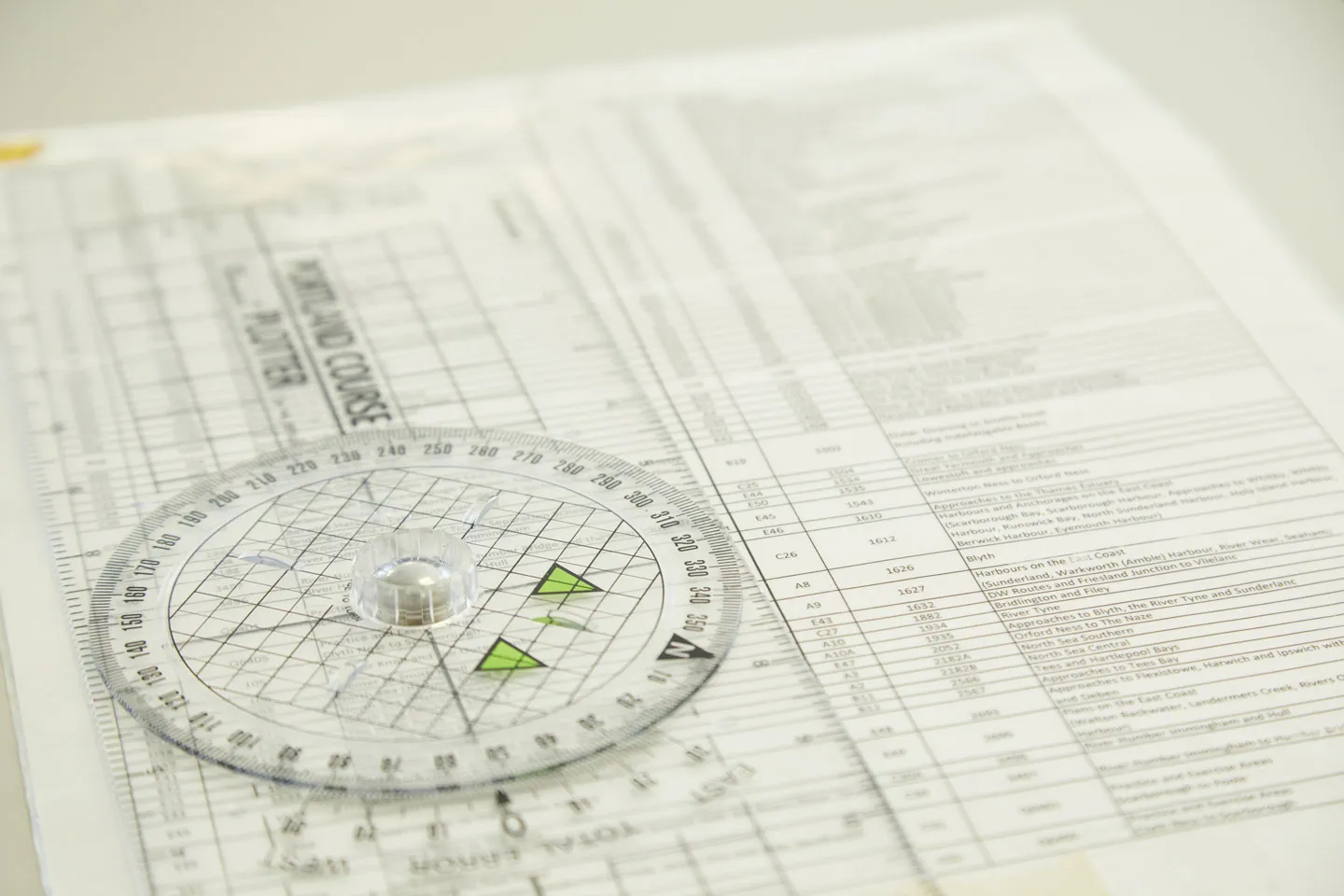 A 360 degree plastic protractor on top of a sheet of paper that includes a list of locations that is mostly blurred
