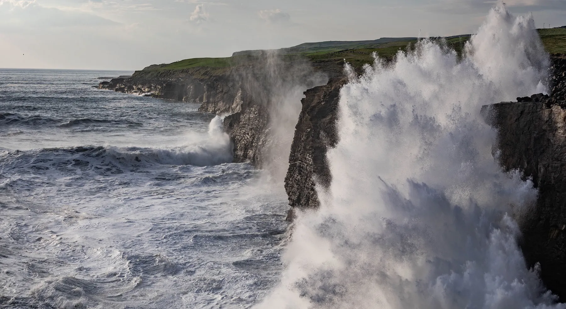 A large wave crashes against cliffs