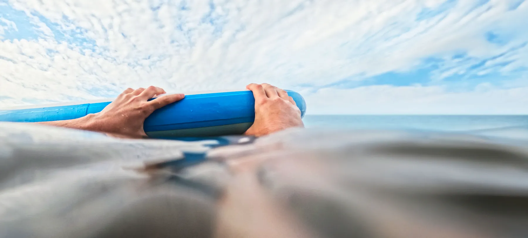A paddleboard in the sea with a pair of hands holding on to it
