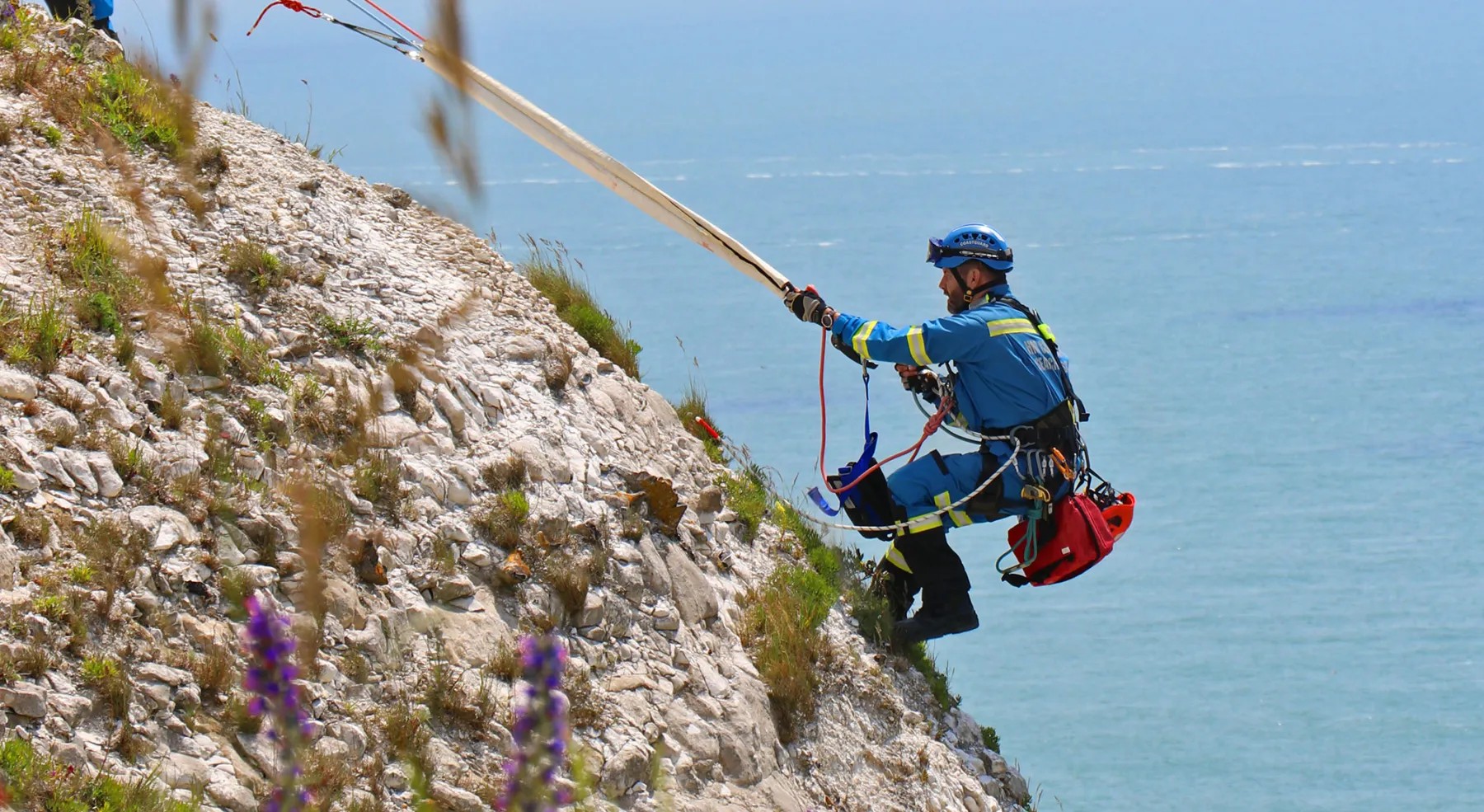 A male coastguard rescue officer descending a cliff on a rope