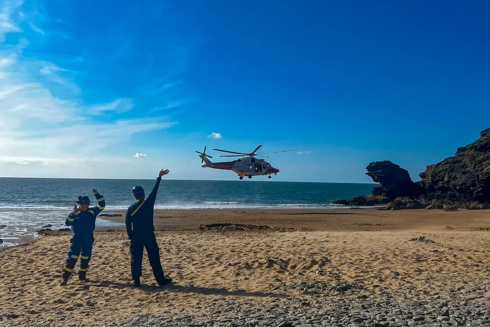 Coastguard rescue officers stood on a sandy beach with helicopter in background