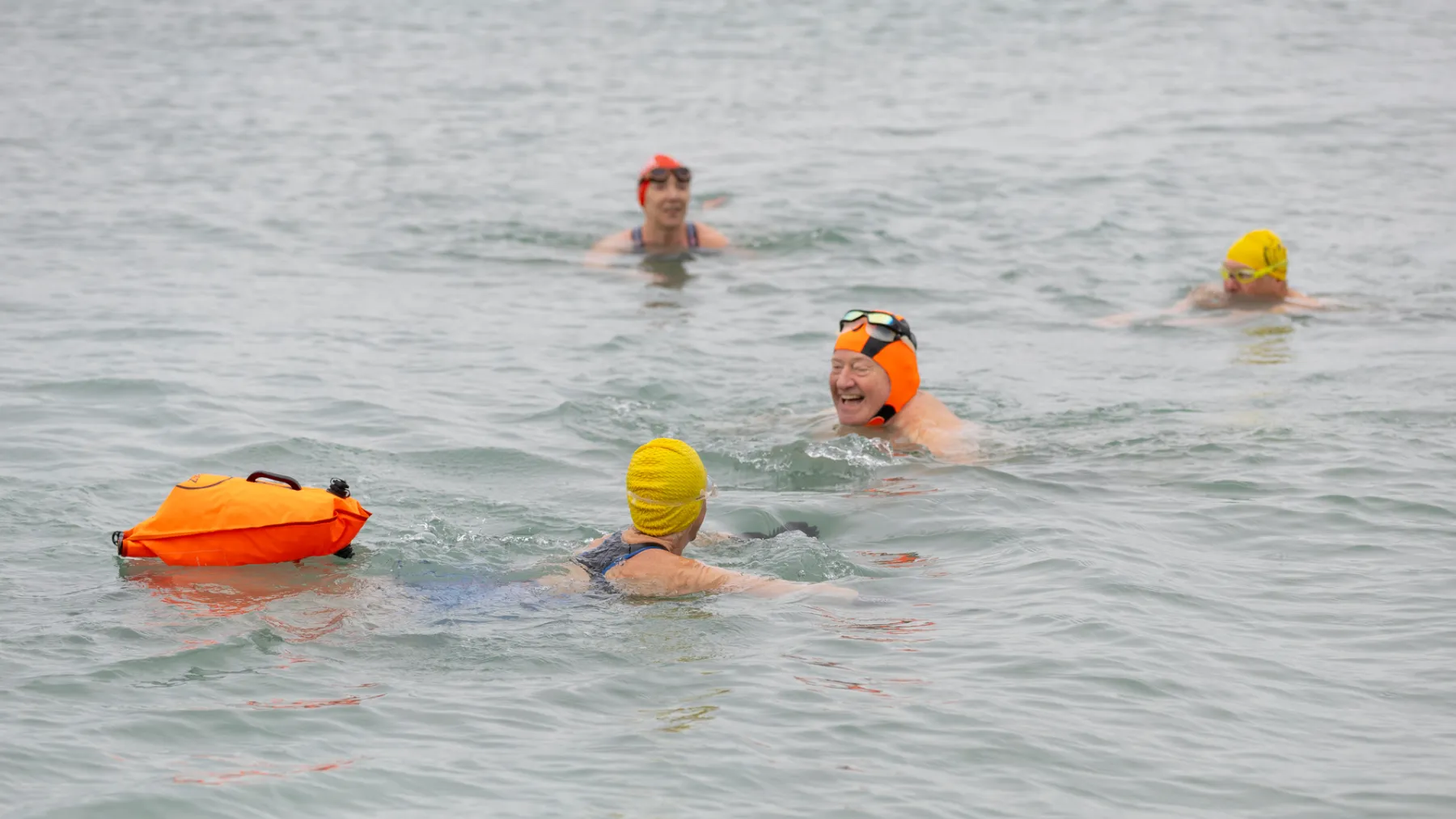 Swimmers in the sea wearing bright headcaps and one towing a float