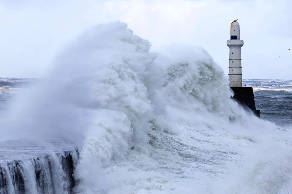 A lighthouse during a storm where large waves are crashing over the walkway