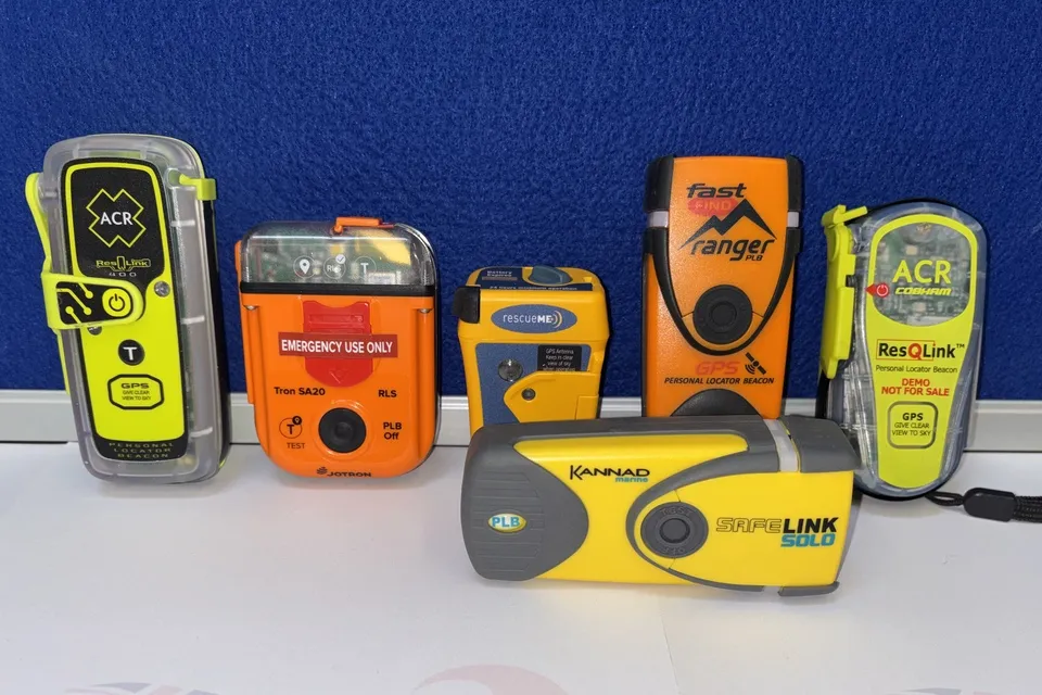 Six different makes of PLB, with colours of bright orange and yellow, are lined up against a blue background