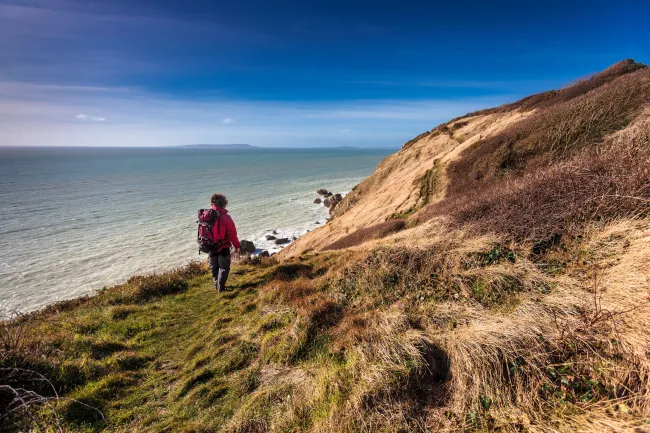 Man in hiking clothes and backpack walking along coastal path with sea in background