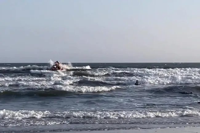 Swimmer in sea with breaking waves and a small lifeboat in distance