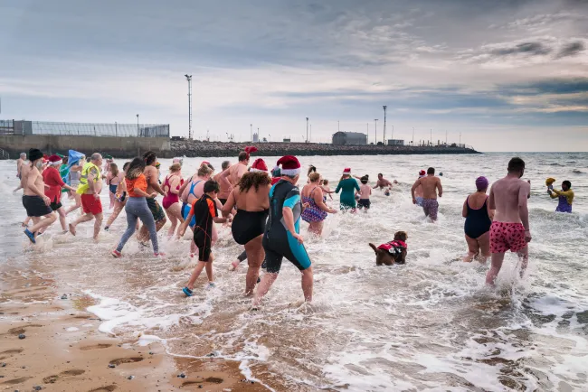 Swimmers running into a wintery sea at Ramsgate, some wearing Christmas hats