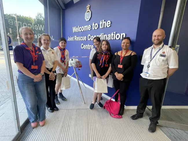 Scouts, parents and coastguards stand in front of the Joint Rescue Coordination Centre entrance sign
