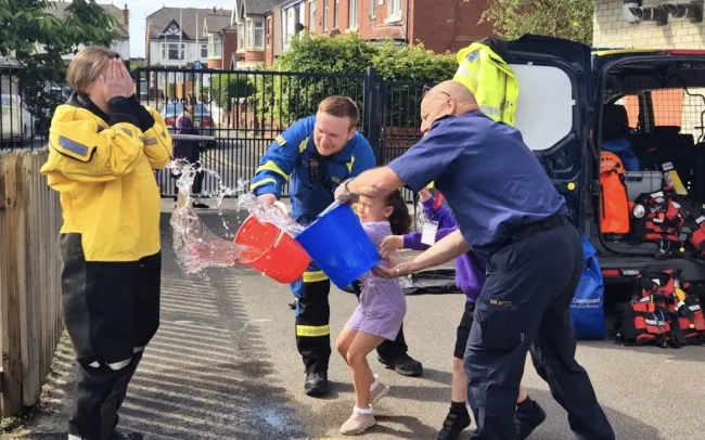 Miss Mills wears HM Coastguard kit as a bucket of water is thrown at her by two coastguards and a pupil