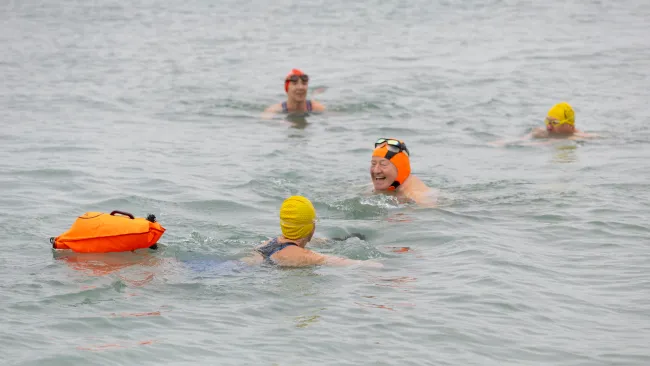 Swimmers in the sea wearing bright headcaps and one towing a float